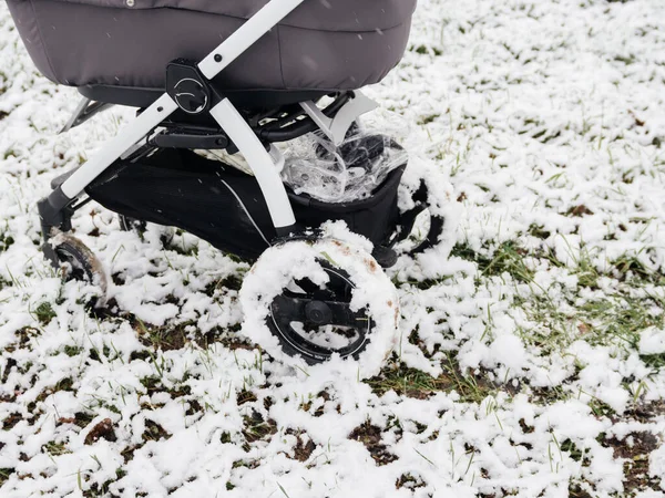 Low angle view of baby stroller carriage with bassinet in the snow field with wheels full from wet snow — Stock Photo, Image