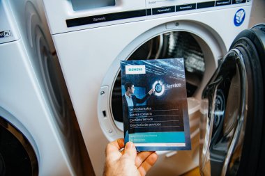 POV erkek eli Bosch Servisi temas broşürü reklamları bilgilendirme rehberi ve arka planda iki yeni Siemens çamaşır ve kurutma makinesi var.