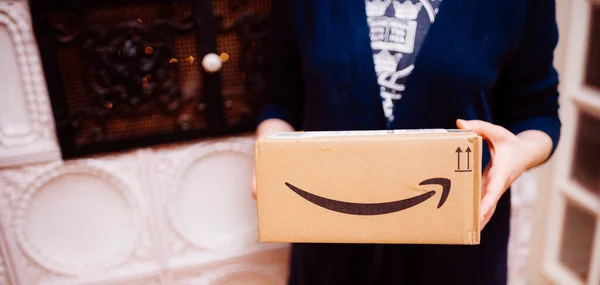 Vista lateral da mulher elegante segurando como um presente um pacote Amazon Prime com sua seta logotipo sorridente com fogão de luxo no fundo — Fotografia de Stock