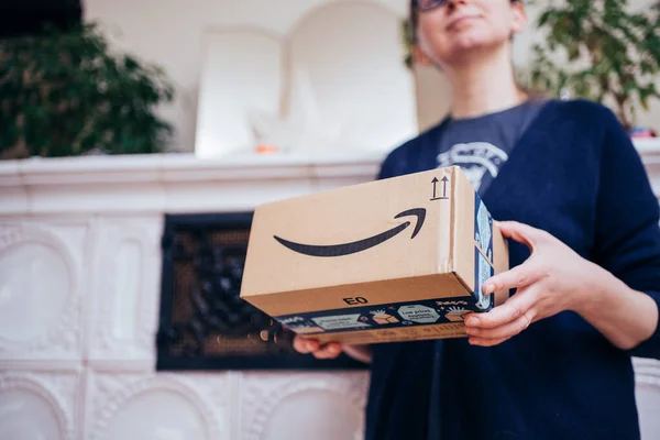 Boční pohled elegantní žena drží jako dárek Amazon Prime balíček s jeho šipkou usmívající se logogram s luxusním sporákem v pozadí — Stock fotografie