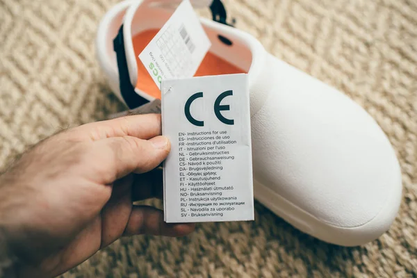 POV mano masculina celebración de papel etiqueta publicitaria de Crocs en el trabajo zapatos cómodos con etiqueta de precio etiqueta con instrucciones de uso —  Fotos de Stock