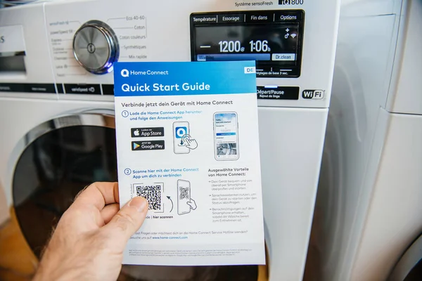 POV Чоловіча рука утримує Bosch Home Connect Quick Start guide з двома останніми Siemens прання і сушіння машини на задньому плані — стокове фото