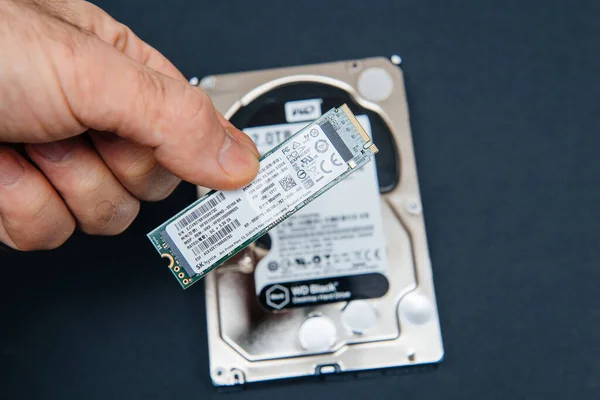 POV male hand holding comparing large HDD hard drive from Western Digital to small NVME SSD M2 disk from SK Hynix — стоковое фото