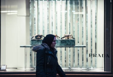 Arap kökenli bir kadın, alacakaranlıkta moda caddesinde lüks Prada çantalarının önünde yürüyor.