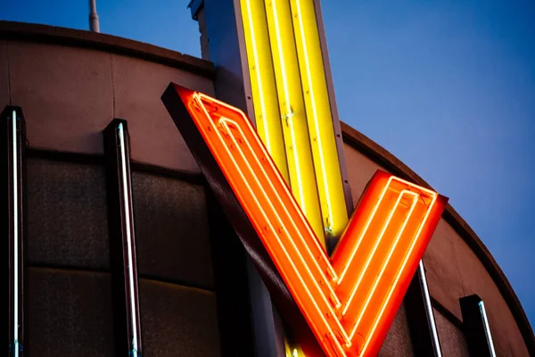 Vintage Neon light tubes forming letter V on the metallic roof top with dusk blue warm color skylight — Stock Photo, Image
