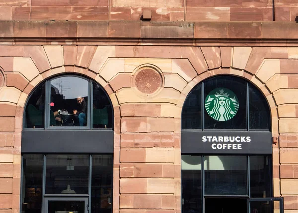 Starbucks kahve logosu binanın ön cephesinde, ikinci katta kahve içen iki kişi var. — Stok fotoğraf