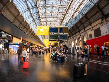 Paris 'teki Gare de Est' te büyük bir kalabalık trenleri beklerken bavullarını toplayıp gazete okuyorlar.