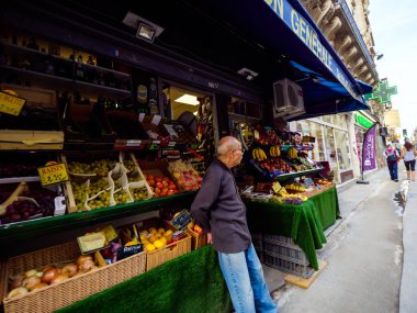 Yalnız Doğulu etnik kökenli bir adam marketinin yanında müşterileri için meyvelerle dolu bir yerde bekliyor. Paris caddesinde organik sebzeler ve meyveler alacaklar.