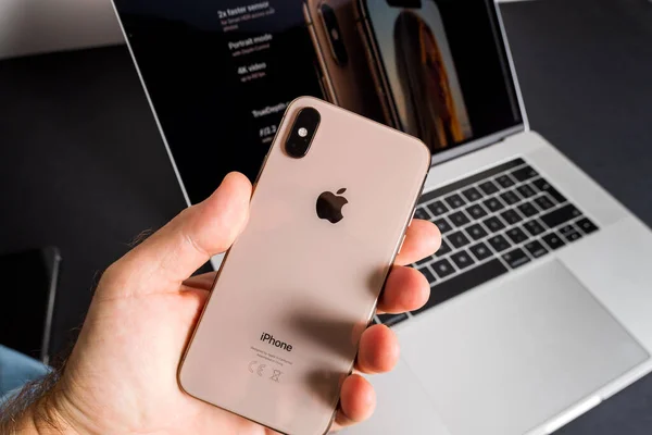 POV mannelijke hand met de nieuwste Apple Computers iPhone Max smartphone met draaiende MacBook Pro op de achtergrond - kijken naar het glazen deel — Stockfoto