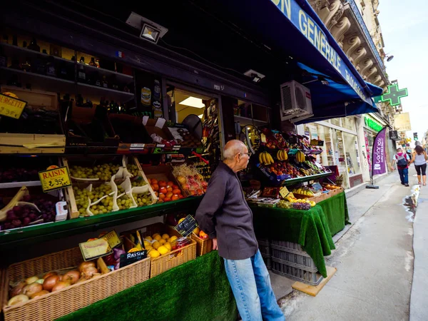 Одинокий восточный этнический человек ждет возле своего рыночного ларька, полного фруктов, чтобы клиенты купили биоорганические овощи и фрукты на парижской улице. — стоковое фото