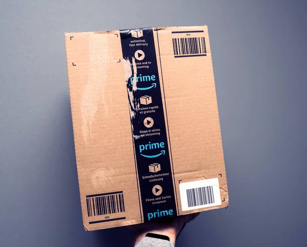 POV männliche Hand hält Amazon Prime Paketkarton vor grauem Hintergrund — Stockfoto