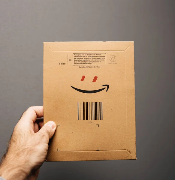 POV mano masculina sosteniendo paquete Amazon Prime sobre con el logotipo de la sonrisa y añadir ojos rojos para formar un personaje humano sonriente — Foto de Stock