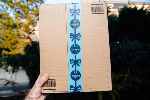 Punto de vista mano masculina sosteniendo mostrando Amazon Prime cartón con cinta adhesiva festiva de vacaciones - fondo de la ciudad desenfocado —  Fotos de Stock
