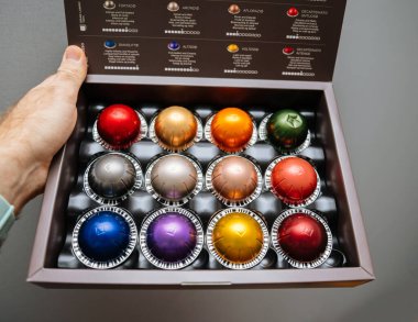 POV male hand holding unboxing new package of with multiple colorful Nespresso coffee capsules, a type of pre-apportioned single-use container of ground coffee beans clipart