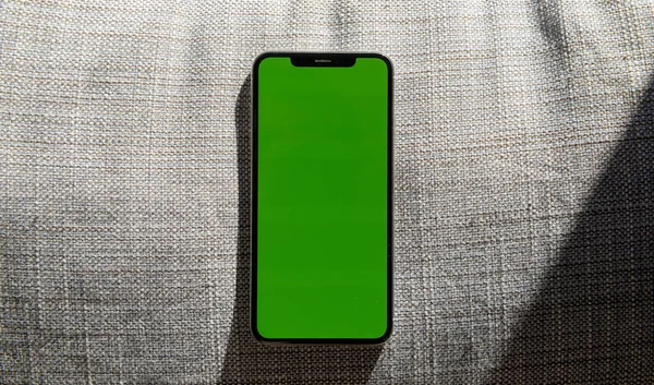 Новий телефон смартфона з зеленим екраном над текстурою сірого одягу — стокове фото