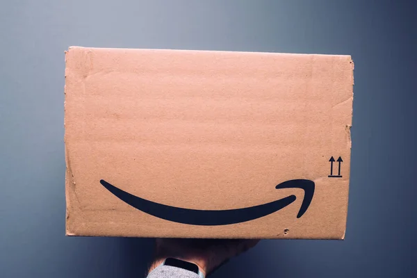 POV male hand holding new package of Amazon prime cardboard parcel delivered with the iconic smile-arrow symbol — Stock Photo, Image