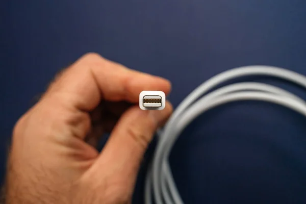 Άντρας κρατώντας γρήγορα Thunderbolt 2 Καλώδιο μήκους 2 μέτρων που κατασκευάζονται από την Apple Computers - απομονώνονται σε μπλε φόντο - εστίαση στο καλώδιο κεφαλής — Φωτογραφία Αρχείου