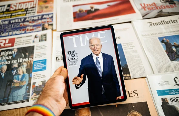 Hombre sosteniendo tableta digital con la portada de la revista Time con Joe Biden y pila con periódicos internacionales — Foto de Stock