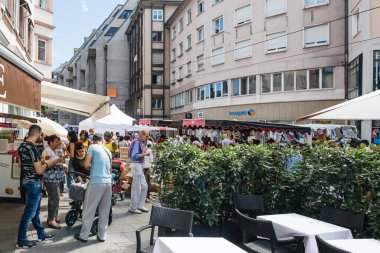 Homme de Fer tramvay istasyonunun ve Grande Braderie caddesindeki fuar fuarı sırasında dükkanların yakınında yürüyen büyük bir kalabalık. Arkadaşları dışarıda bira içiyor.