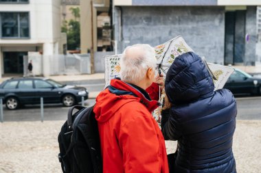 Lizbon sokaklarında şemsiyeyi açmaya çalışan tanınmayan iki yaşlı adam ve kadın.