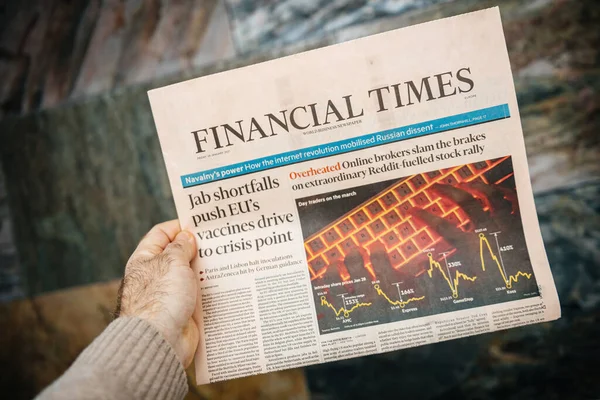 POV male hand holding Financial Times newspaper reading about the Reddit stock rally and anti covid Vaccine crisis — Stock Photo, Image