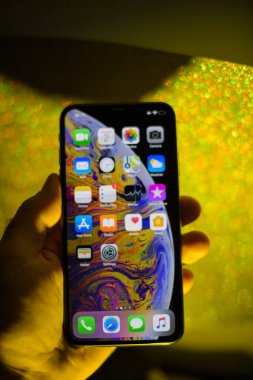 Yeni Apple Bilgisayarları iPhone XS 111 12 profesyonel son model altın parıltılı arka plana karşı odaklanmış POV erkek eli