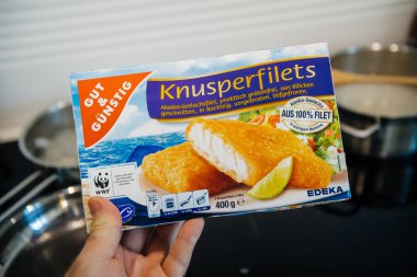 POV erkek eli edeka Gut und Gunstig geleneksel knusperfilet 'ten donmuş balıklarla dolu yeni bir paket tutuyor - mutfak arka planı