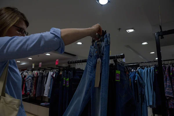 Mujer de compras en el interior de la tienda para un nuevo par de vaqueros - la medición en el aire de la ropa de mezclilla bio azul de lujo —  Fotos de Stock