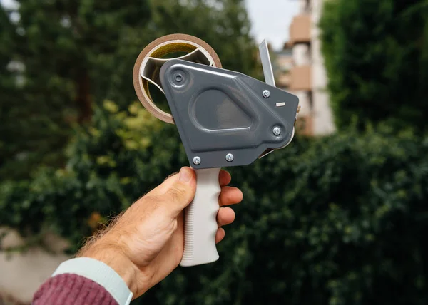 Mano masculina sosteniendo contra fondo verde nuevo dispensador de cinta adhesiva con cinta adhesiva escocesa — Foto de Stock