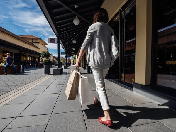 Vista trasera de la mujer soltera caminando por el callejón con múltiples tiendas en el Roppenheim El estilo Outlet sosteniendo bolsas de papel con Aigle y otras marcas — Foto de Stock