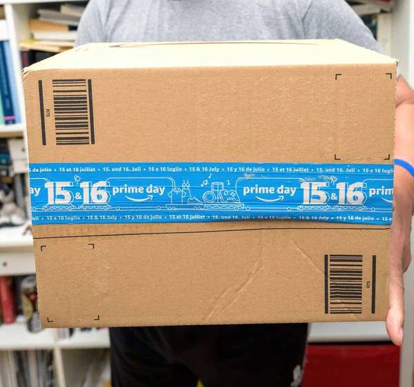 Senior handen met nieuwe Amazon Prime pakket logotype met de glimlachende pijl en Prime Day 15-16 scotch tape - het internet conglomeraat opgericht door Jeff Bezos in een garage in 1994 — Stockfoto