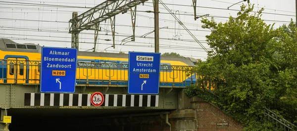 Szybki pociąg holenderski przejeżdżający na moście z drogowskazem do Alkmaar, Bloemendaal, Zandvoort i w kierunku stacji docelowej do Utrechtu i Amsterdamu — Zdjęcie stockowe