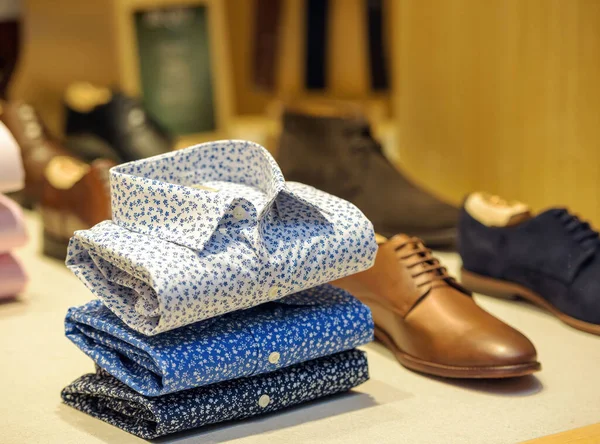 Male floral shirts next to leather shoes for sale in showcase of a modern store — Stock Photo, Image