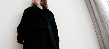 Beyaz duvara yaslanmış siyah yünlü bir kadın.