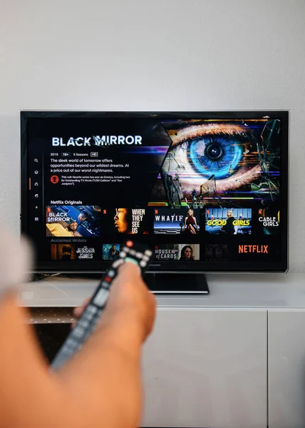 Mão masculina sênior segurando controle remoto olhando para o novo Plasma Panasonic TV com Netflix e Black Mirror página de introdução — Fotografia de Stock