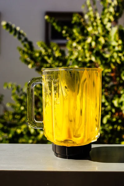 Glazen blender met gele vloeistof binnen op de vensterbank — Stockfoto