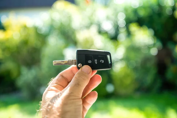 POV male hand holding new car key against green defocused background — Stock Photo, Image
