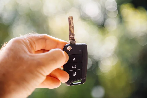 Male hand holding new car key against green defocused background — Stock Photo, Image