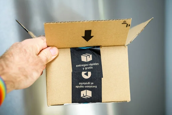 POV personal perspective male hand holding Amazon prime cardboard package carton box with free and fast delivery sticker — Stock Photo, Image