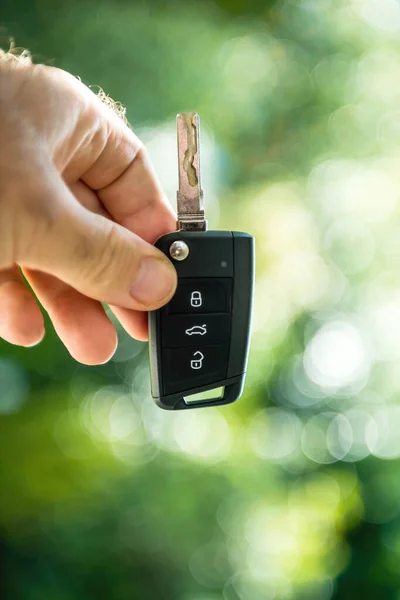 Vertical image - POV male hand holding new car key against green defocused background — Stock Photo, Image