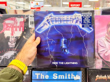 Berlin, Almanya - Mar 6, 2025: Bir Alman müzik dükkanında Ride the Lightning 'in plak plağını elinde tutan kişi, Death, The Smiths ve Sabbath Black gibi diğer albüm kapaklarını da içeriyor.