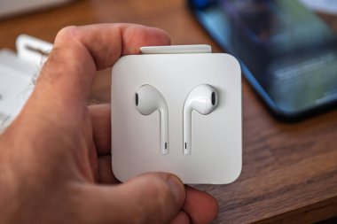 Paris, Fransa - Sep 2, 2025: Kutu açılırken USB-C konnektörlü yeni Apple Earpod 'ları tutmak, arka planda bulanık iPhone, kablo aksesuar ve ürün tasarımı.