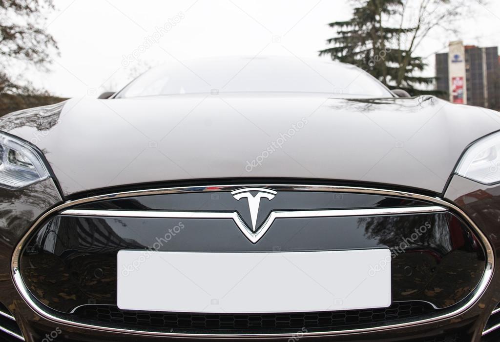 PARIS, FRANCE - NOV 29, 2014: Luxury Tesla frontal view of badge head-lights and logo are seen below the hood of the Model S electric vehicle on European city street