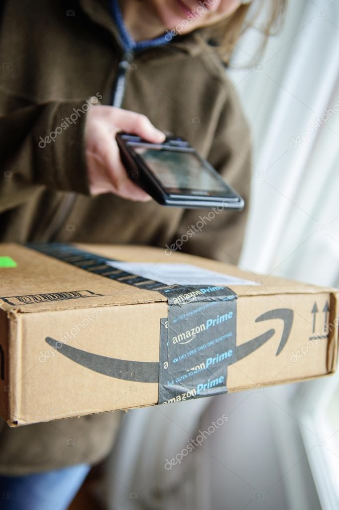 PARIS, FRANCE - JAN 27, 2016: Smiling UPS United Parcel Service young female postal delivery courier scanning the ontime delivering package from Amazon Prime