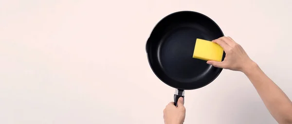 Asian man in grey color T shirt cleaning the non stick pan with handy dishwashing sponge which yellow color on the soft side and green on hard side for hygiene after cook and white background studio shot