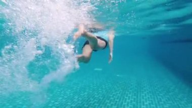 Asyalı güzel bir kızın su altında yavaşça yüzme havuzunun diğer tarafına yüzmesi. Kameraya su sıçratan beyaz hava kabarcıkları ve suyun altında mavi renkler. Spor eğlencesi konsepti.