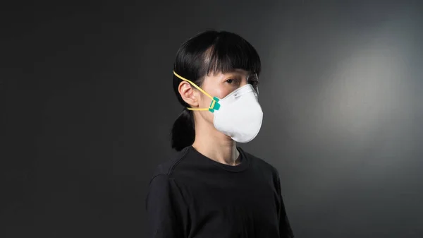 Asian girl in a mask on a black background in Coronavirus Quarantine situation. Title about the outbreak of the corona virus in the World, illness. Epidemic. female wearing N95 mask studio black background