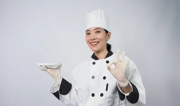シェフのジェスチャー ポートレート美しいアジアの女性は 帽子をかぶって調理し シェフの制服はジェスチャーサインを作り カメラを見ています インフルエンサー 料理教室 コピースペース オンライン食品商人のシェフ — ストック写真