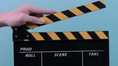 Alkış tahtası. Kapalı el ele tutuşmalar, boş siyah ve sarı şeritli filmler, mavi yeşil arka plan stüdyosundaki film şeridini izole eder. Aralıklı olarak alkışladı. video üretimi için film tahtası.