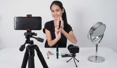 Güzellik blogcusu. Asyalı genç bir kadın kameranın önünde oturur ve canlı yayında güzellik blogu yazarı ya da youtuber olarak evde barışma hakkında yorum ya da tavsiyelerde bulunur. Stüdyo beyaz arkaplan.